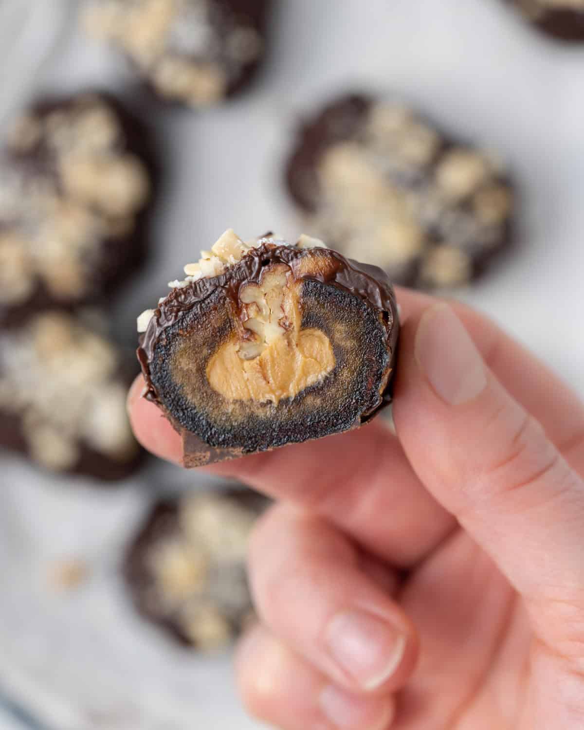 A hand holding a a halved chocolate-covered date Snickers.
