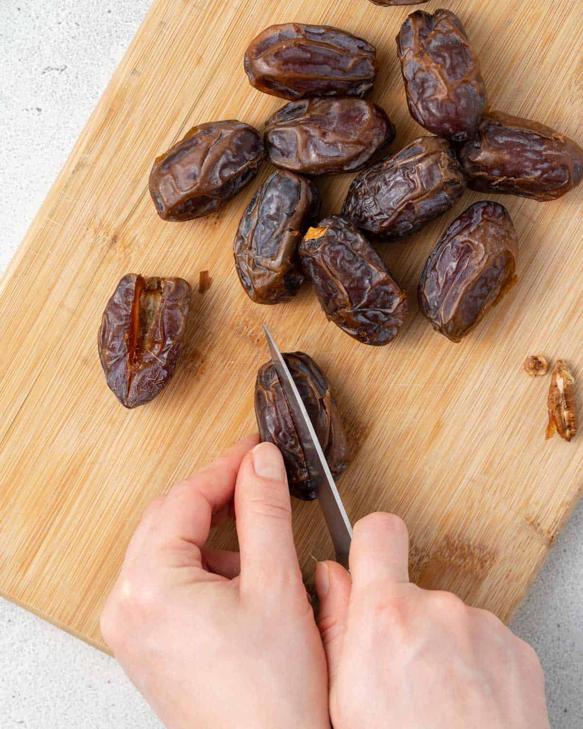 A hand with a knife slicing open a date to remove the pit.