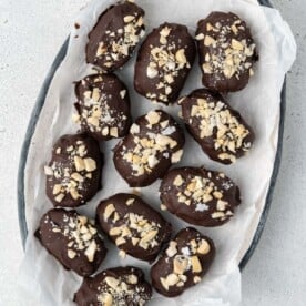 date snicker bites coated in chocolate and topped with chopped peanuts added on a plate.
