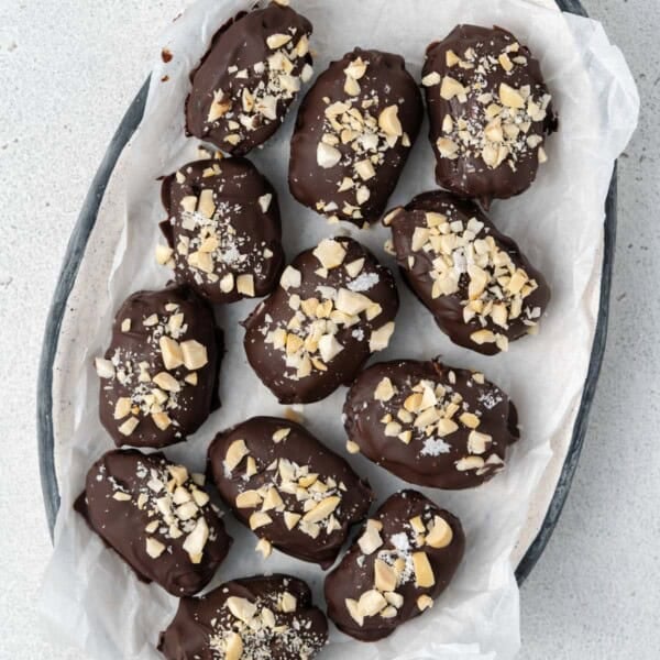 date snicker bites coated in chocolate and topped with chopped peanuts added on a plate.