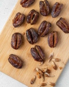 A cutting board with halved, pitted dates next to the date stones.
