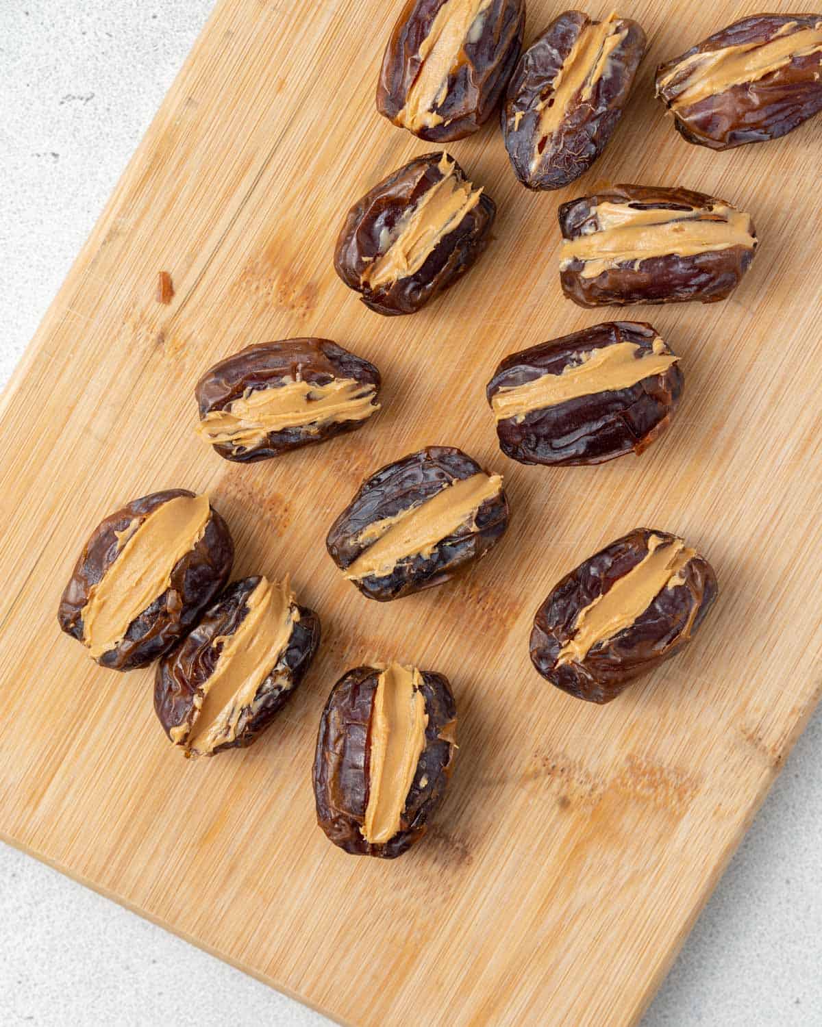 A cutting board with halved, pitted dates with peanut butter in them.