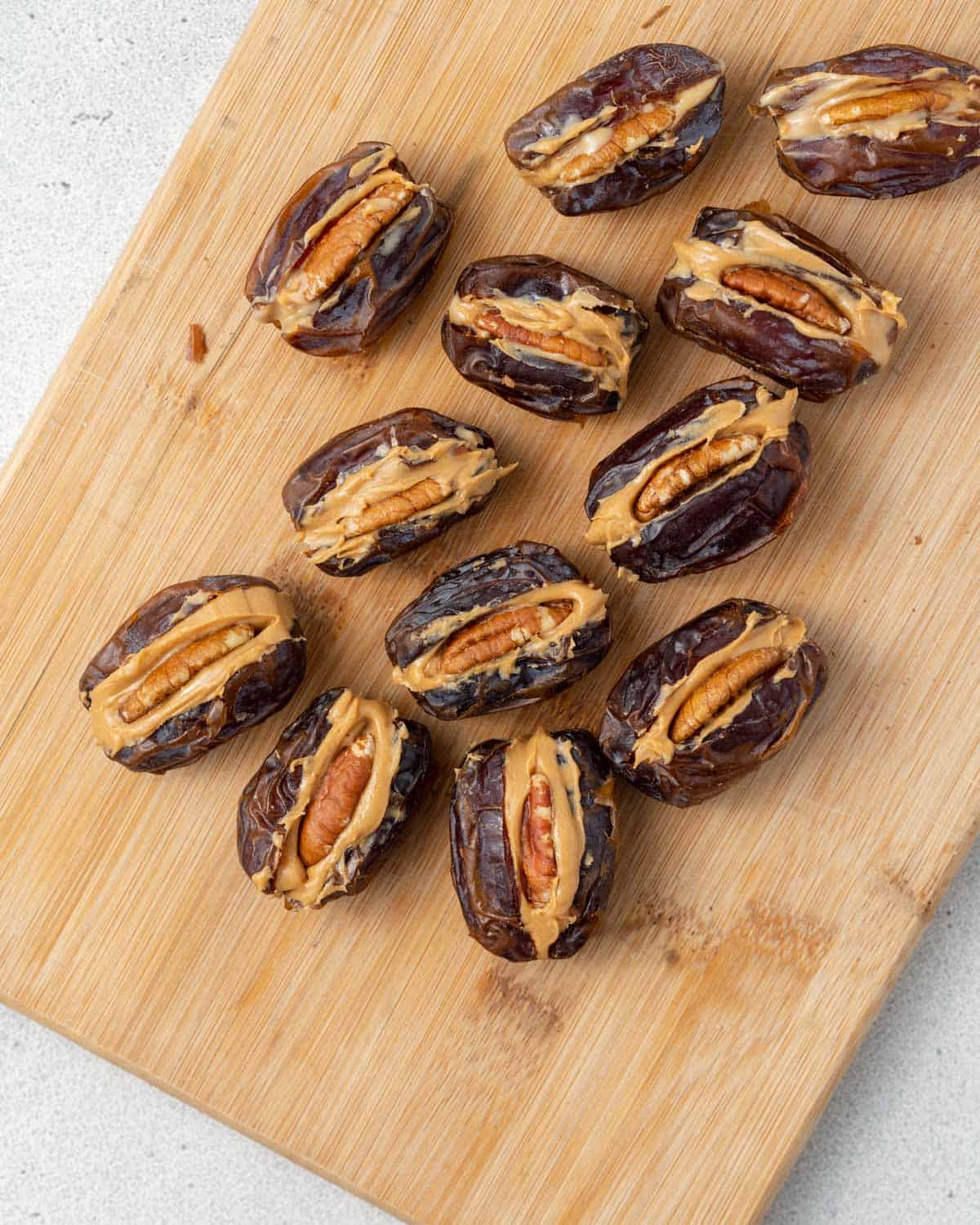 A cutting board with stuffed dates arranged before dipping, filled with peanut butter and pecans