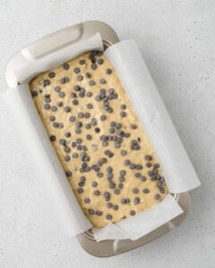 Banana bread batter is added to a pan and topped with chocolate chips.