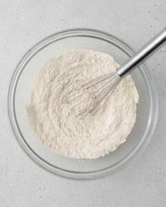 Flour, baking powder, baking soda, cinnamon, and salt, whisked in a bowl.