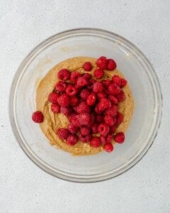 Raspberries added over batter in a bowl.