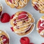raspberry muffins on a flat surface topped with a drizzle if icing sugar.