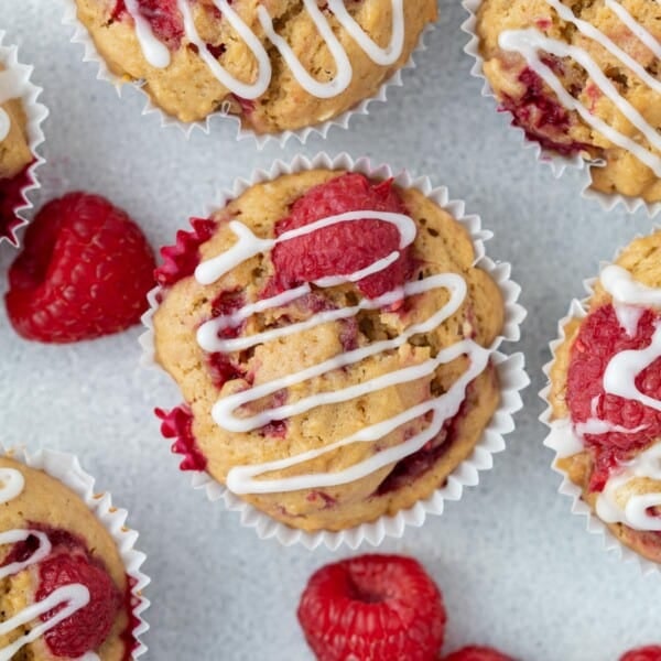 raspberry muffins on a flat surface topped with a drizzle if icing sugar.