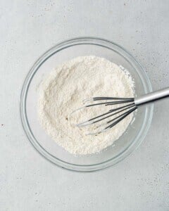 Flour and baking powder are being whisked in a bowl.