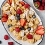 Scrambled pancakes on an oval dish topped with powdered sugar and berries.