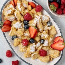 Scrambled pancakes on an oval dish topped with powdered sugar and berries.