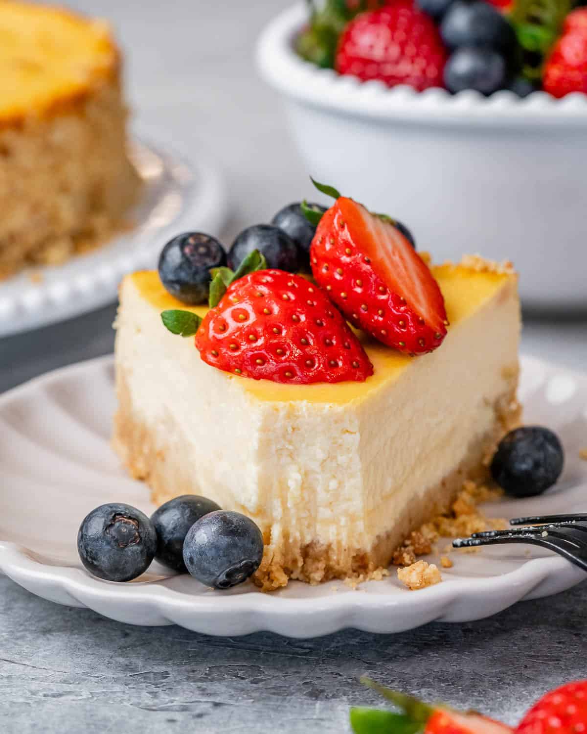 Slice of cottage cheese cheesecake topped with strawberries and blueberries on a white plate.