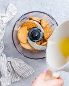 Melted butter being poured into food processor with broken graham crackers in it.