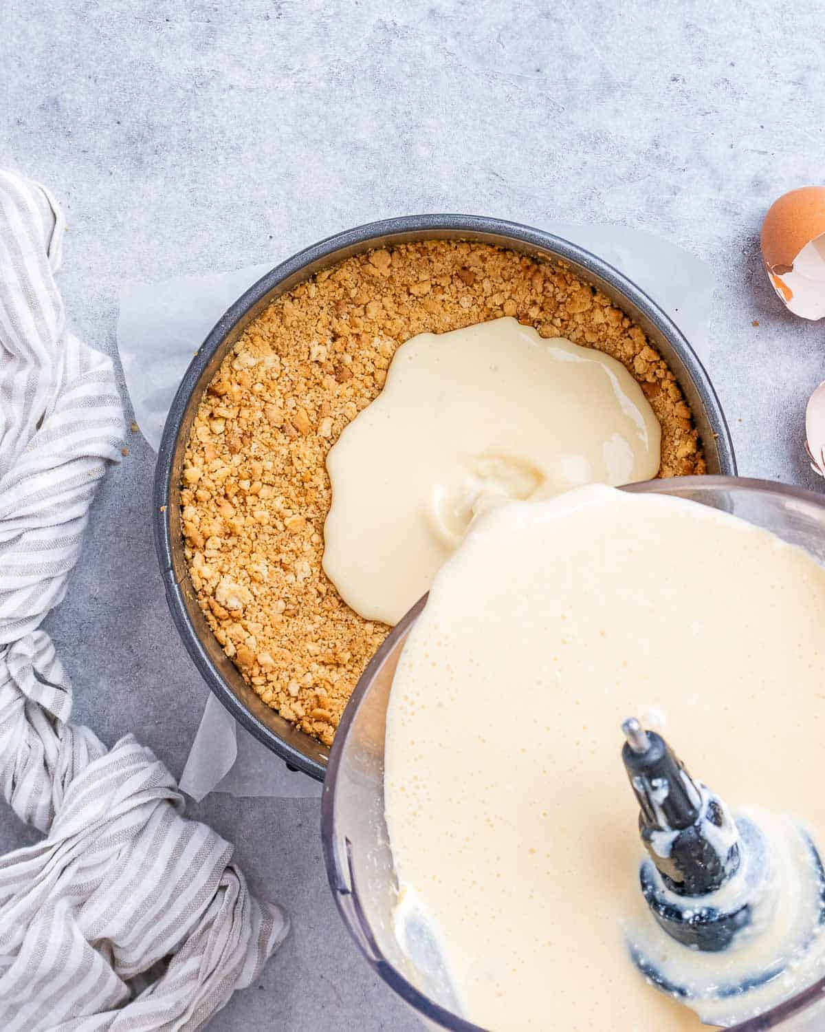 Cheesecake filling being poured into crust in a round baking pan.