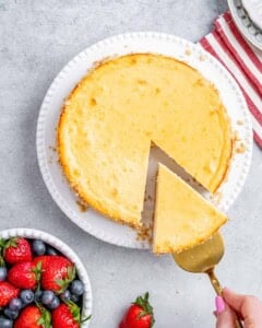 Whole baked cheesecake with one slice cut out, sitting next to fresh berries.