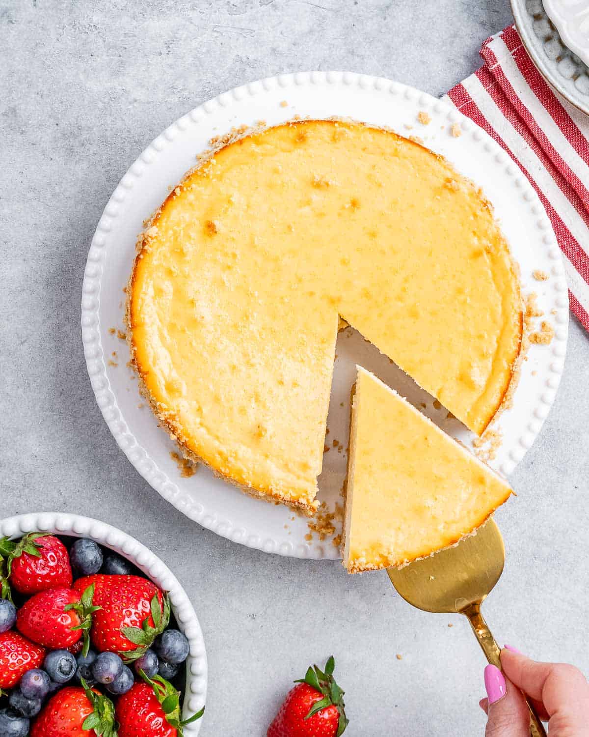 Whole baked cheesecake with one slice cut out, sitting next to fresh berries.