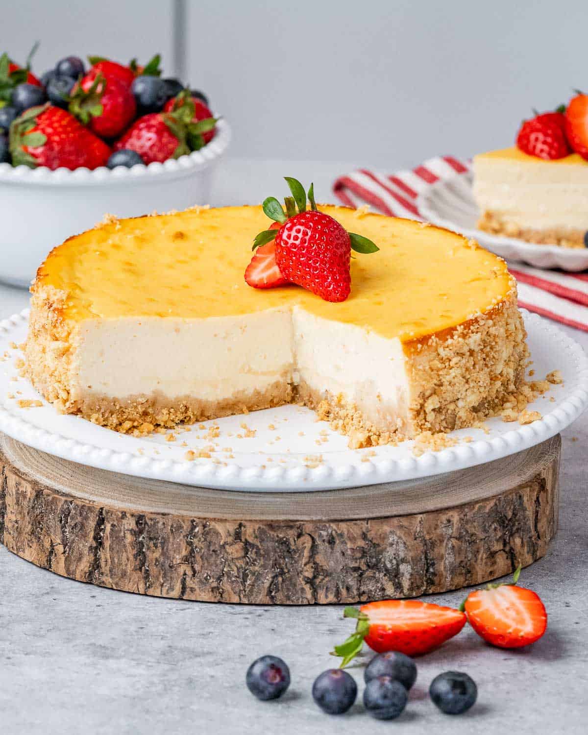 Full cheesecake on a wooden platter, topped with strawberries.