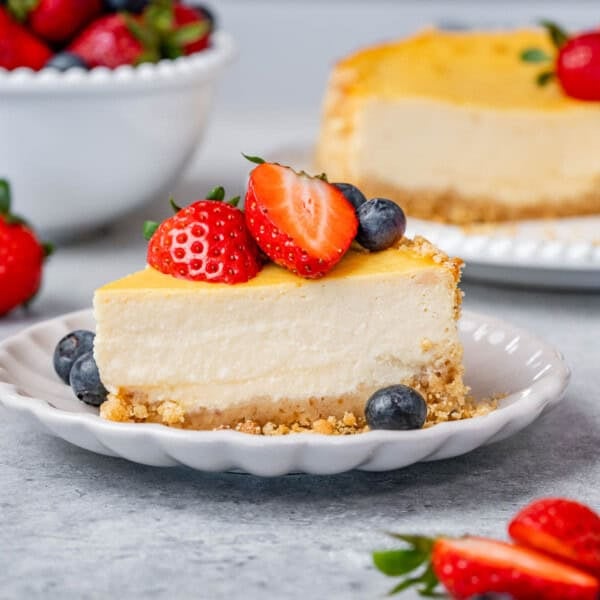 Slice of cheesecake on a plate with strawberries, blueberries, and a strawberry half on top.