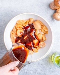 Pouring red sauce over raw chicken pieces in a white bowl.
