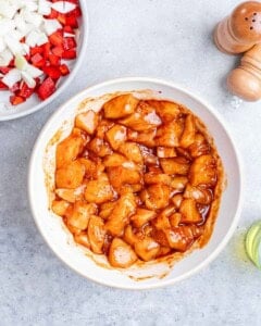 Raw, seasoned chicken pieces in a white bowl.
