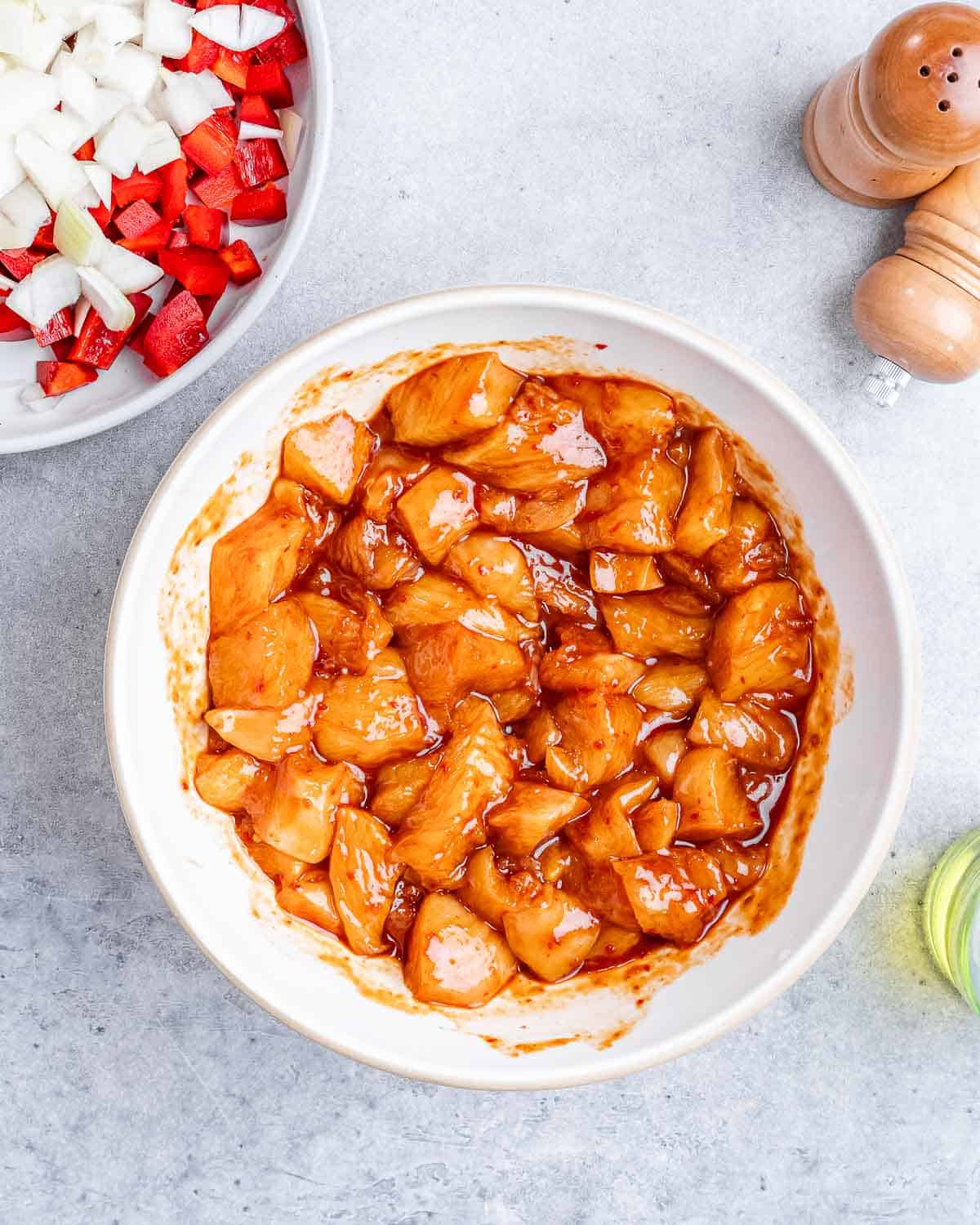 Raw, seasoned chicken pieces in a white bowl.