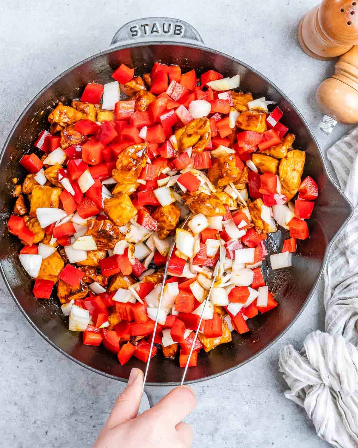 Tongs stirring chicken and vegetables in a skillet.