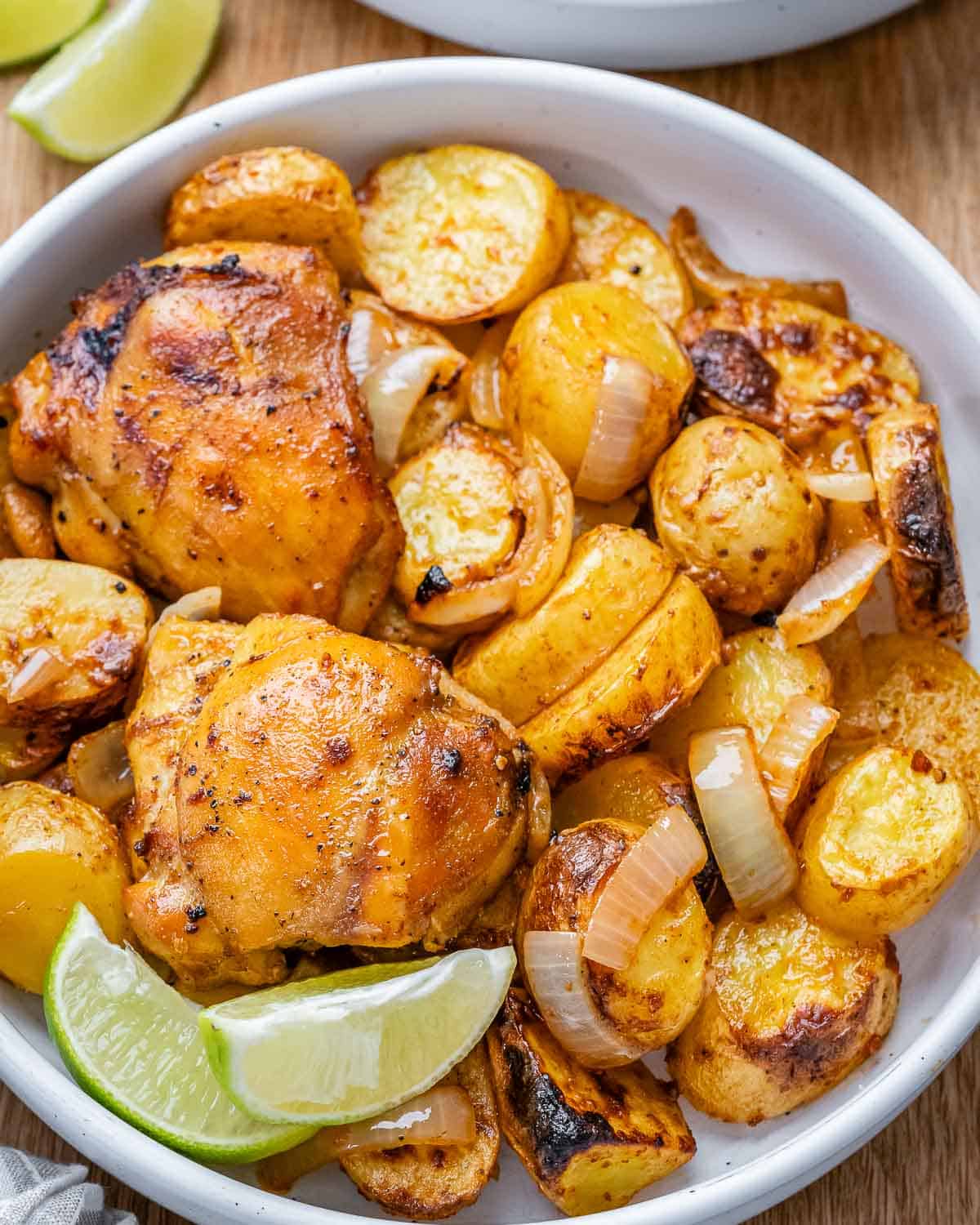 Close-up of crispy, golden potatoes and baked chicken thighs nestled together in a bowl.