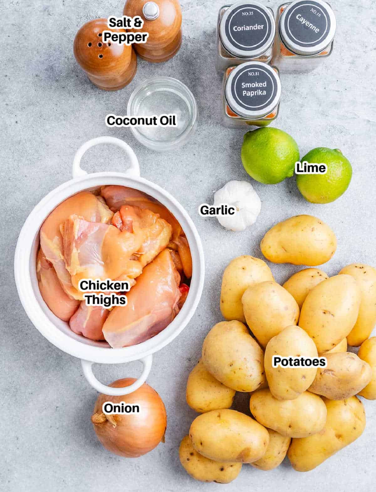 Overhead shot of raw ingredients (chicken, potatoes, lime, garlic, coconut oil, and onion) labeled and laid out on a clean surface.