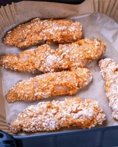 Breaded but uncooked chicken tenders on parchment paper, arranged in a single layer and ready for the air fryer.