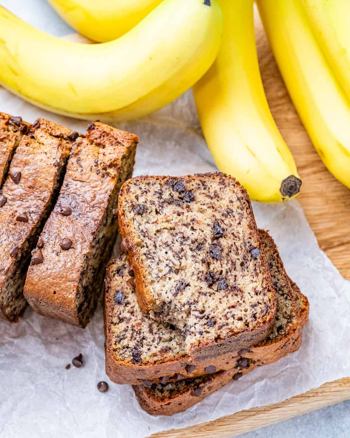 Four slices of almond flour banana bread stacked next to bananas with one slice angled forward.