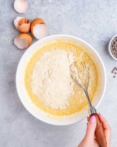 Mixing bowl with almond flour being whisked into wet ingredients for banana bread batter.