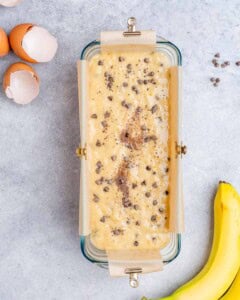 Loaf pan filled with banana bread batter topped with chocolate chips, ready to be baked.
