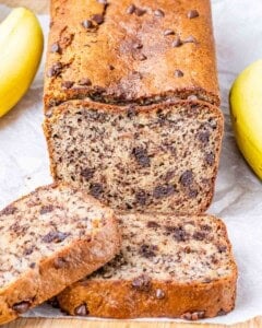 Close-up of freshly baked almond flour banana bread loaf with a golden brown crust, surrounded by bananas.