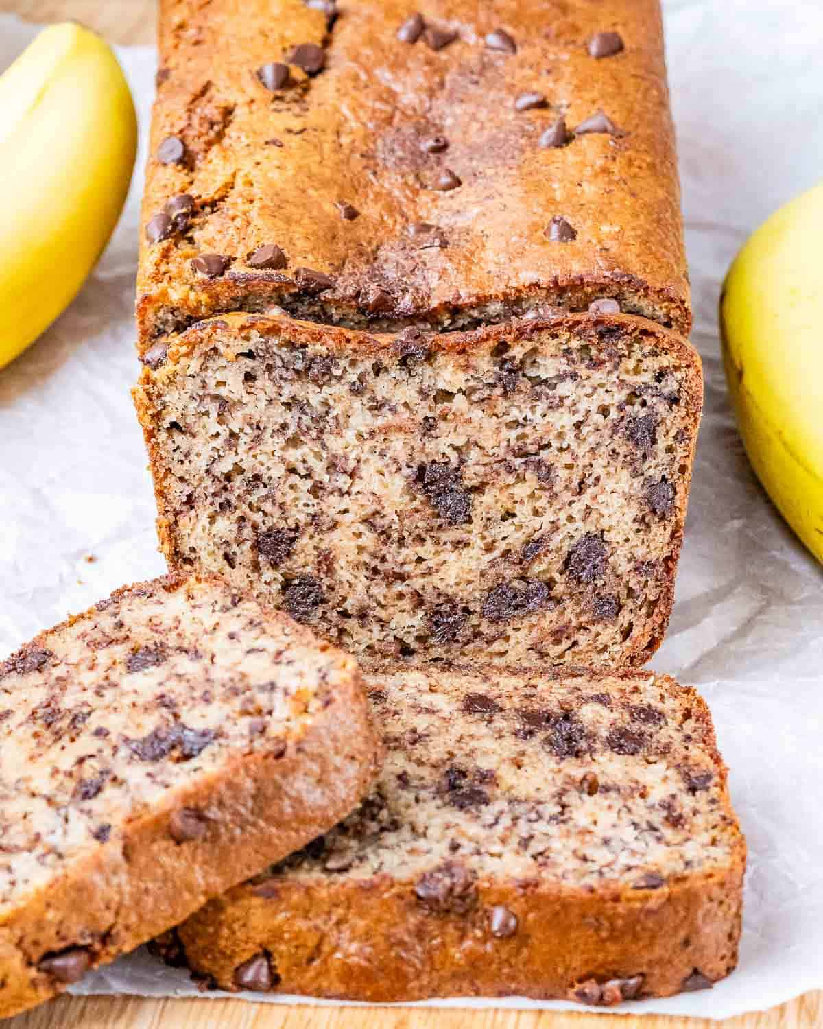 Close-up of freshly baked almond flour banana bread loaf with a golden brown crust, surrounded by bananas.