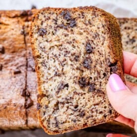 Hand holding a slice of banana bread to show soft interior packed with chocolate chips.