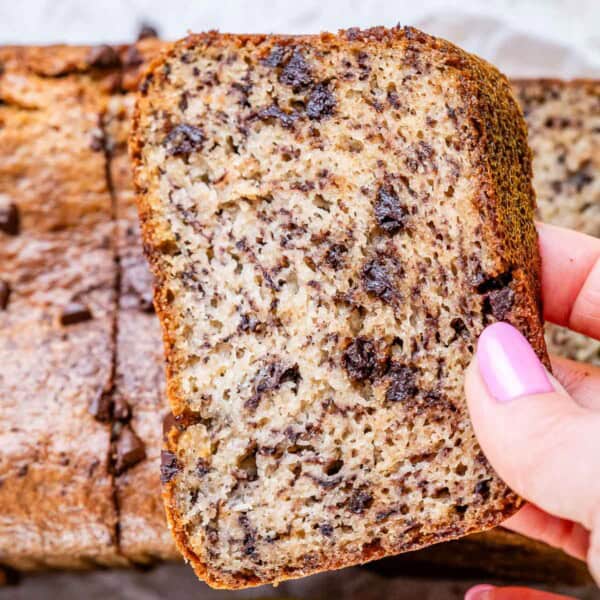 Hand holding a slice of banana bread to show soft interior packed with chocolate chips.