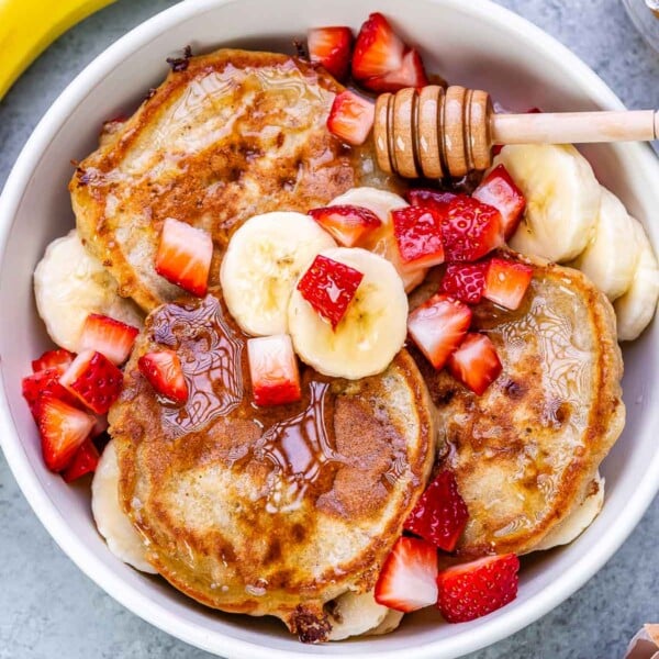 pancakes in a bowl topped with sliced bananas and chopped strawberries.