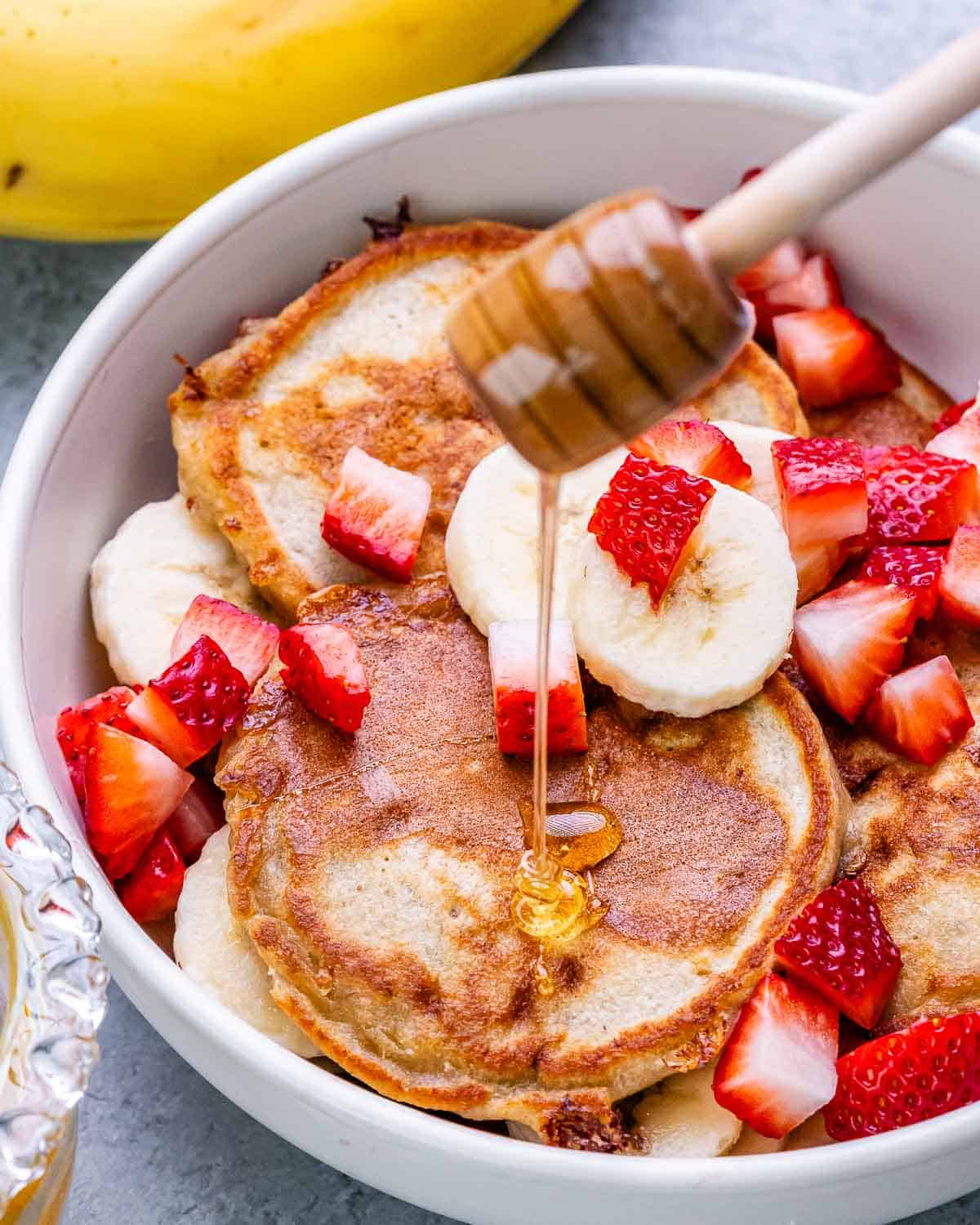 Drizzling honey on cottage cheese pancakes with sliced banana and strawberry