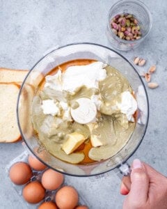 Overhead shot of ingredients in a food processor, including butter, pistachio butter, cream cheese, and honey, ready to blend for the custard base of a brioche French toast casserole.
