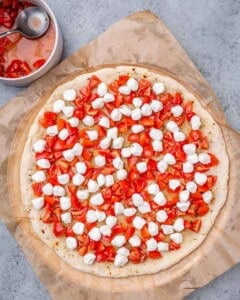 Pizza crust topped with mozzarella pearls and diced tomatoes, ready to bake.