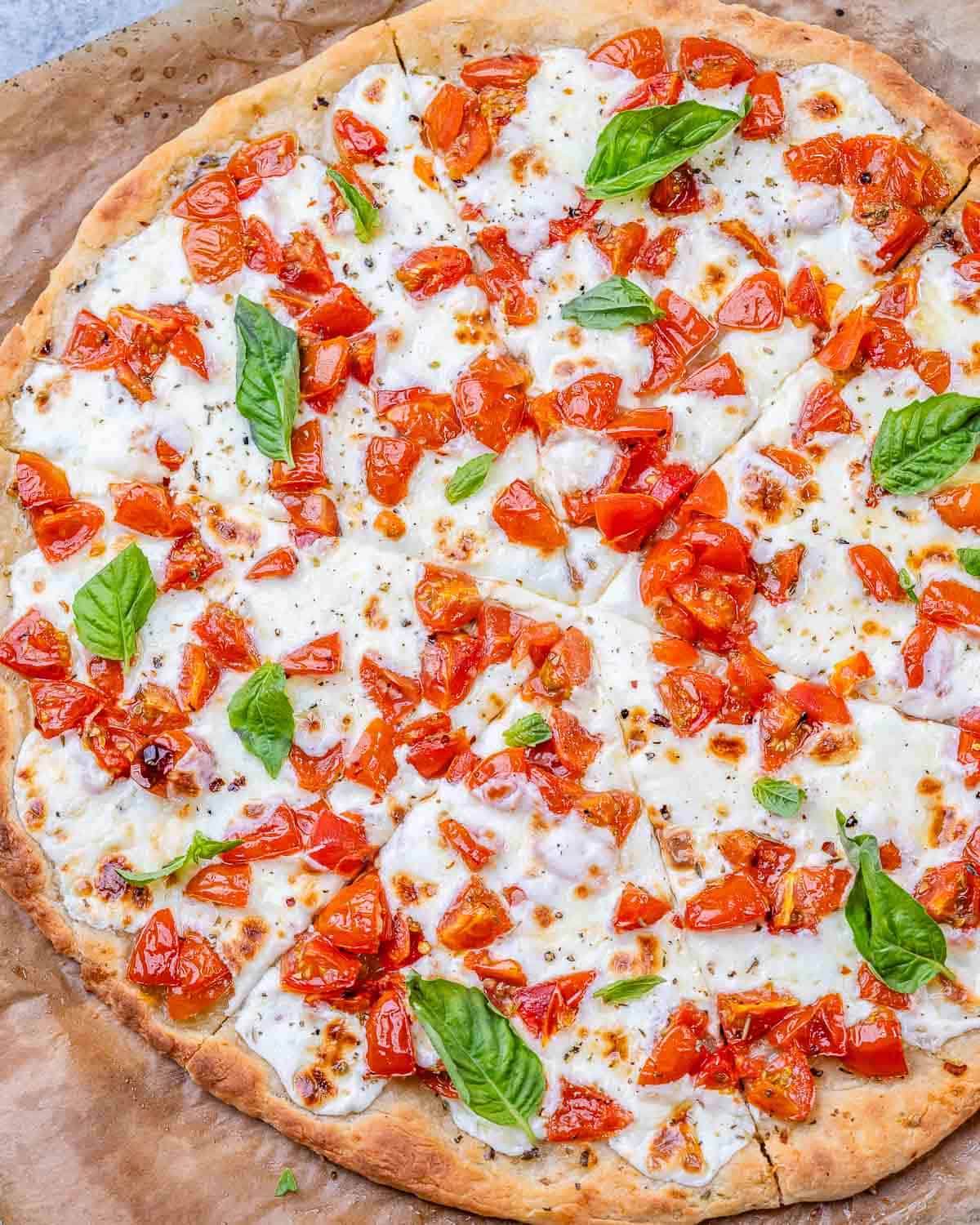 Top view of the whole pizza, showing the tomato and cheese topping with fresh basil leaves throughout.