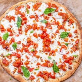 Overhead shot of the full bruschetta pizza with visible seasoning and basil scattered across the top.