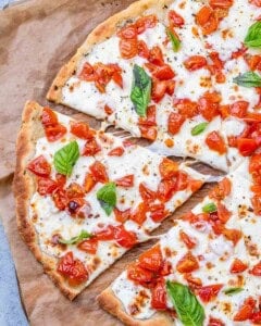 Whole baked bruschetta pizza topped with melted mozzarella, tomatoes, and fresh basil, centered in frame.