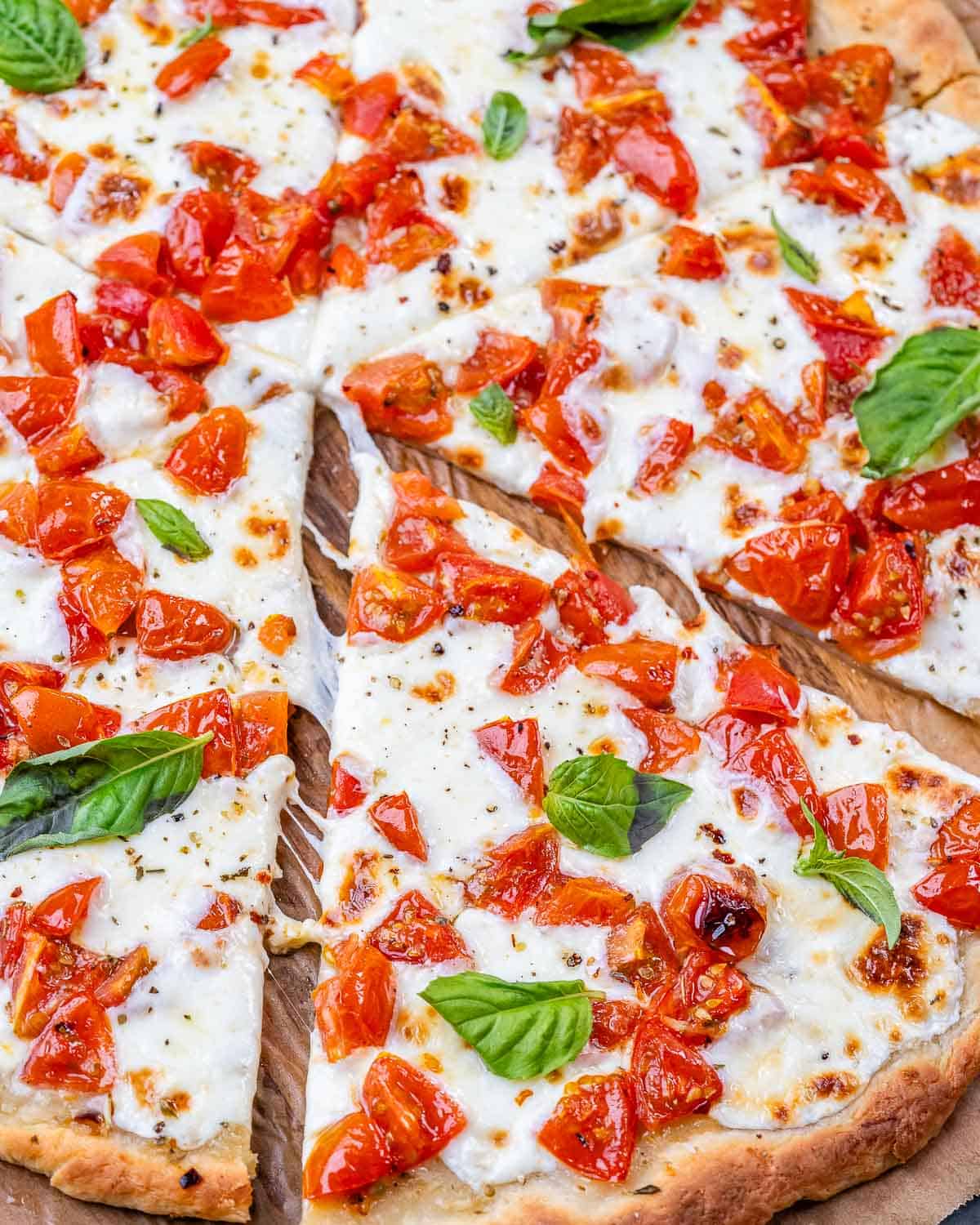 Finished bruschetta pizza with basil leaves, cut into slices, viewed from above.