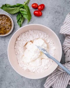 Mixing bowl filled with flour and yogurt being stirred with a spatula on a gray surface.