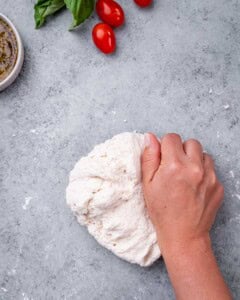 Hand kneading pizza dough on a lightly floured surface.