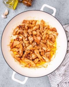 Cooked chicken pieces browning in a skillet with oil and seasoning.
