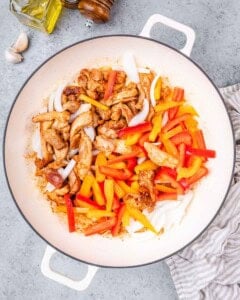 Sautéed chicken added to a plate with sliced red and orange bell peppers.