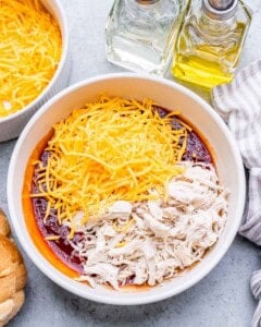 Shredded cheese and chicken on top of sauce ingredients in a bowl.