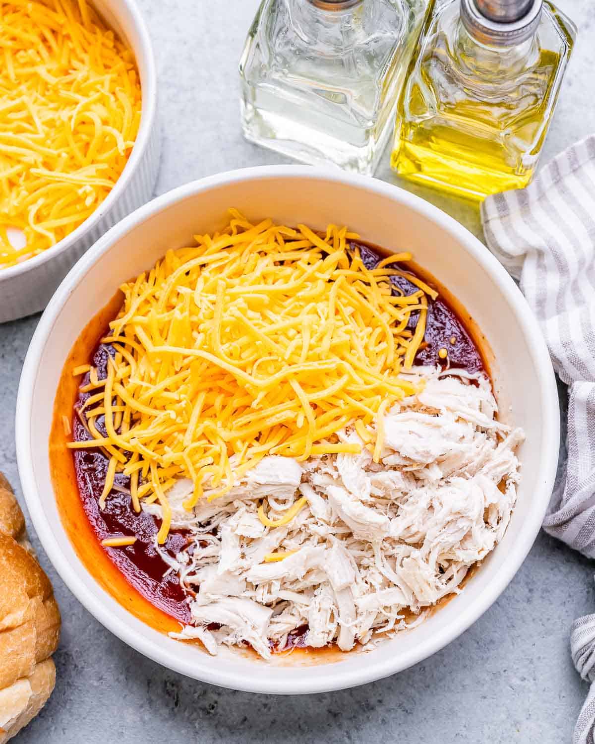 Shredded cheese and chicken on top of sauce ingredients in a bowl.